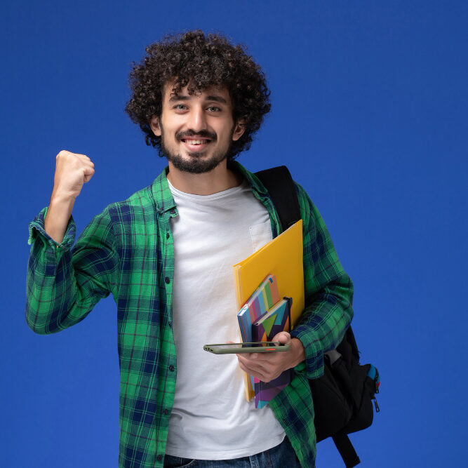 front-view-male-student-wearing-black-backpack-holding-copybook-files-using-his-phone-light-blue-wall